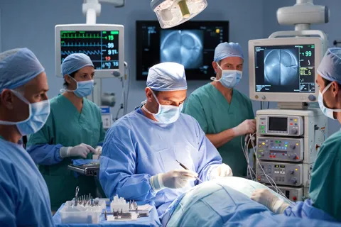 Equipo médico realizando un cateterismo cardíaco en sala de hemodinamia, con fluoroscopia en pantalla.