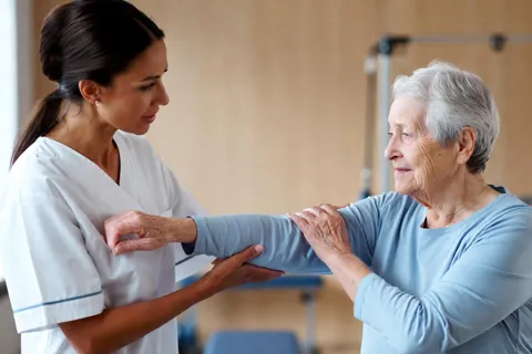 Fisioterapeuta trabajando con un paciente cardíaco mayor en una sesión de rehabilitación, realizando ejercicios suaves de movilidad.
