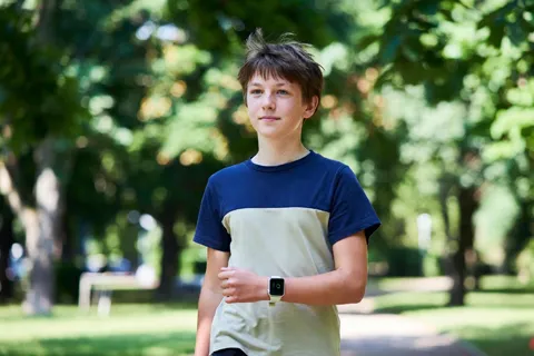 Joven caminando suavemente en un parque, monitoreando su ritmo cardíaco con reloj inteligente, durante recuperación post-miocarditis.